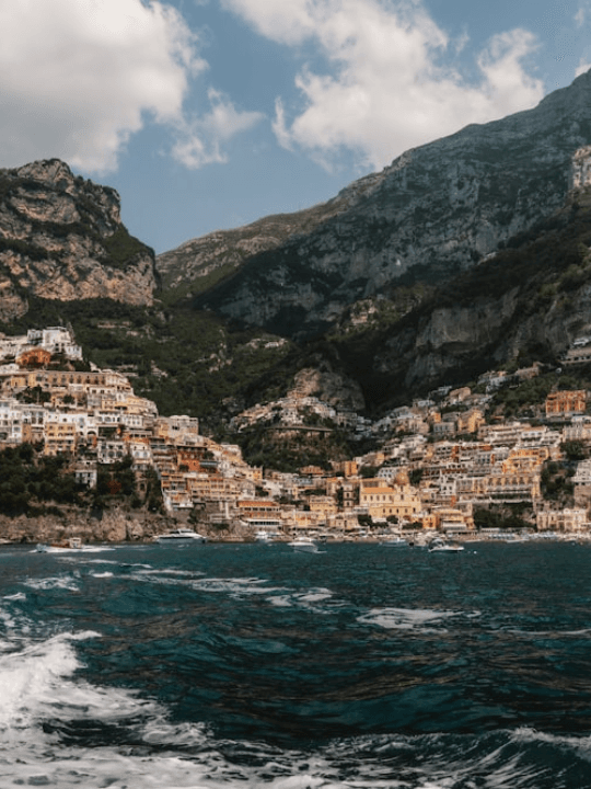 A sunlit coastal village framed by mountains and the Mediterranean Sea